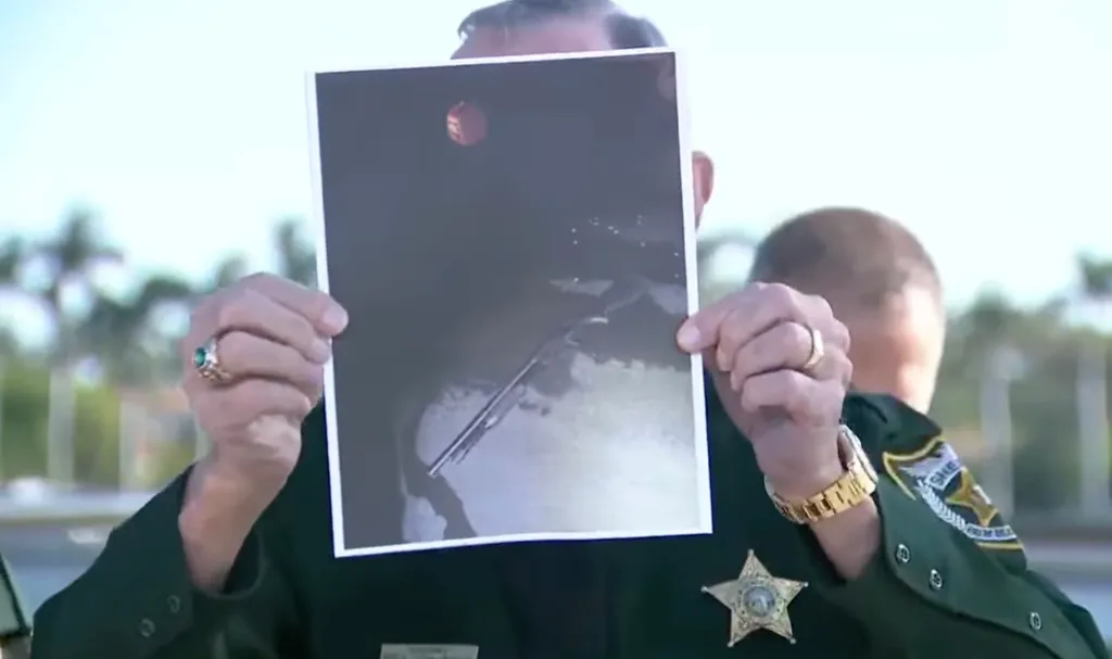 A man in a sheriff's uniform holds up a photo of a gun in water.
